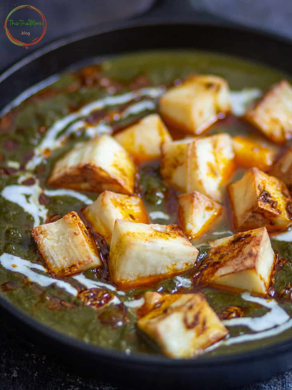 Palak Paneer served in a black pan with a drizzle of tempering.