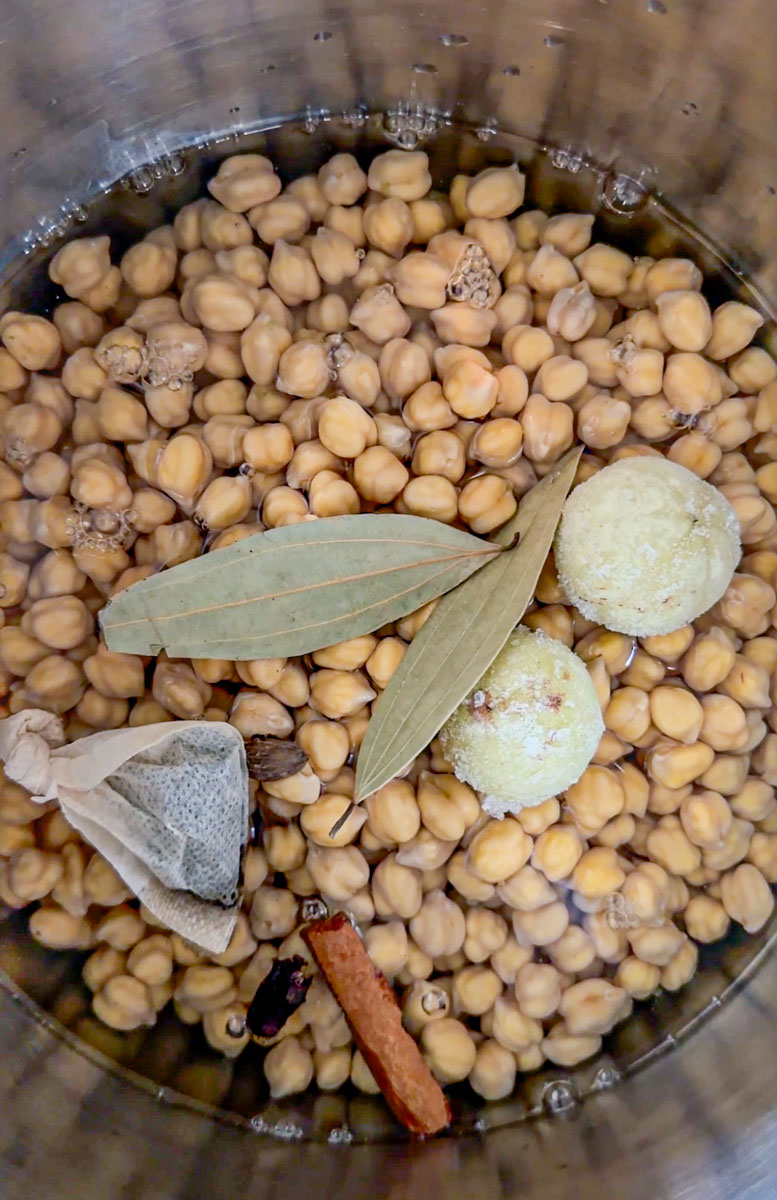 Chickpeas cooking with tea bag and whole spices in a pot.