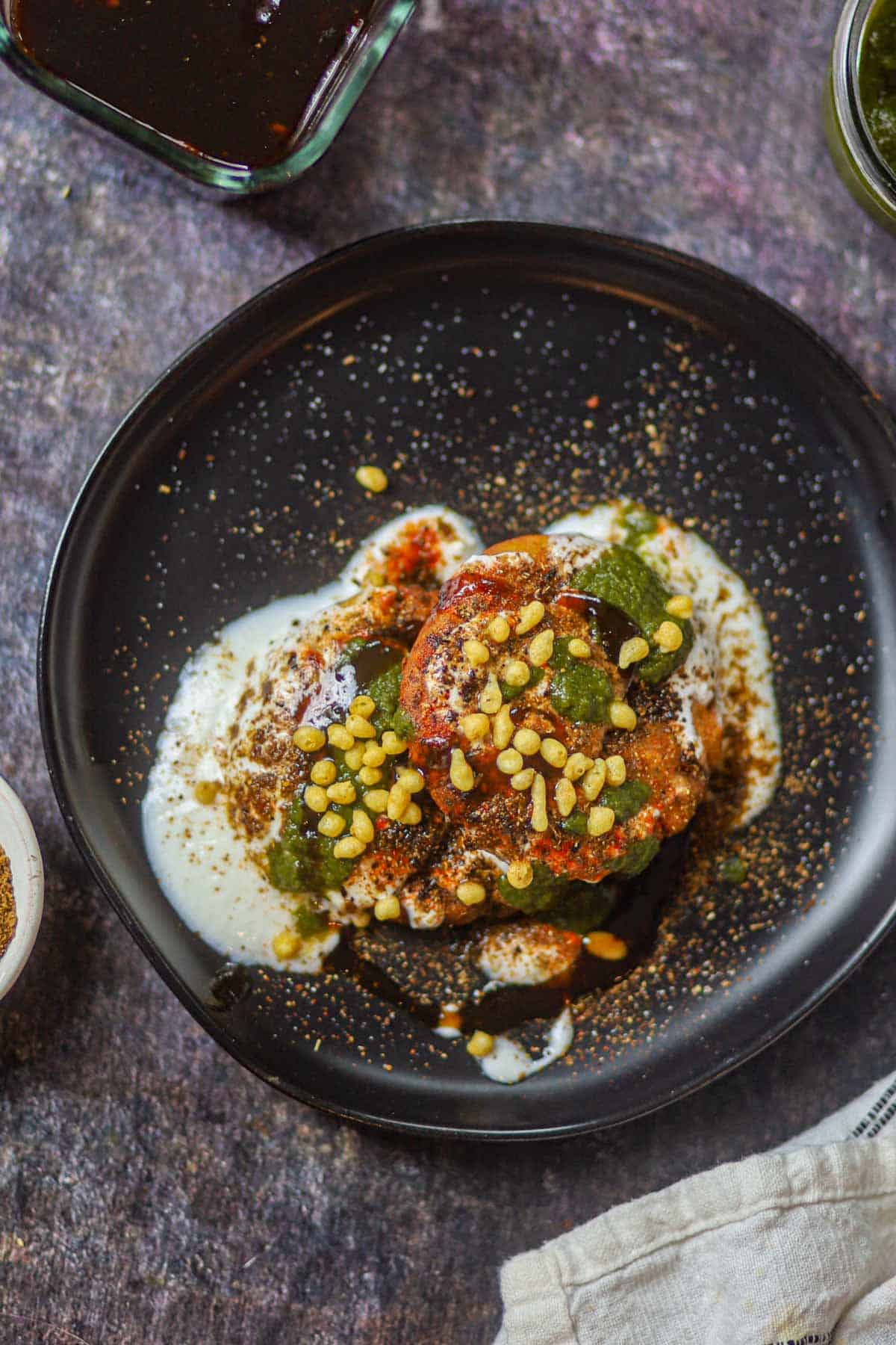 Overhead view of aloo tikki chaat with yogurt and chutneys.