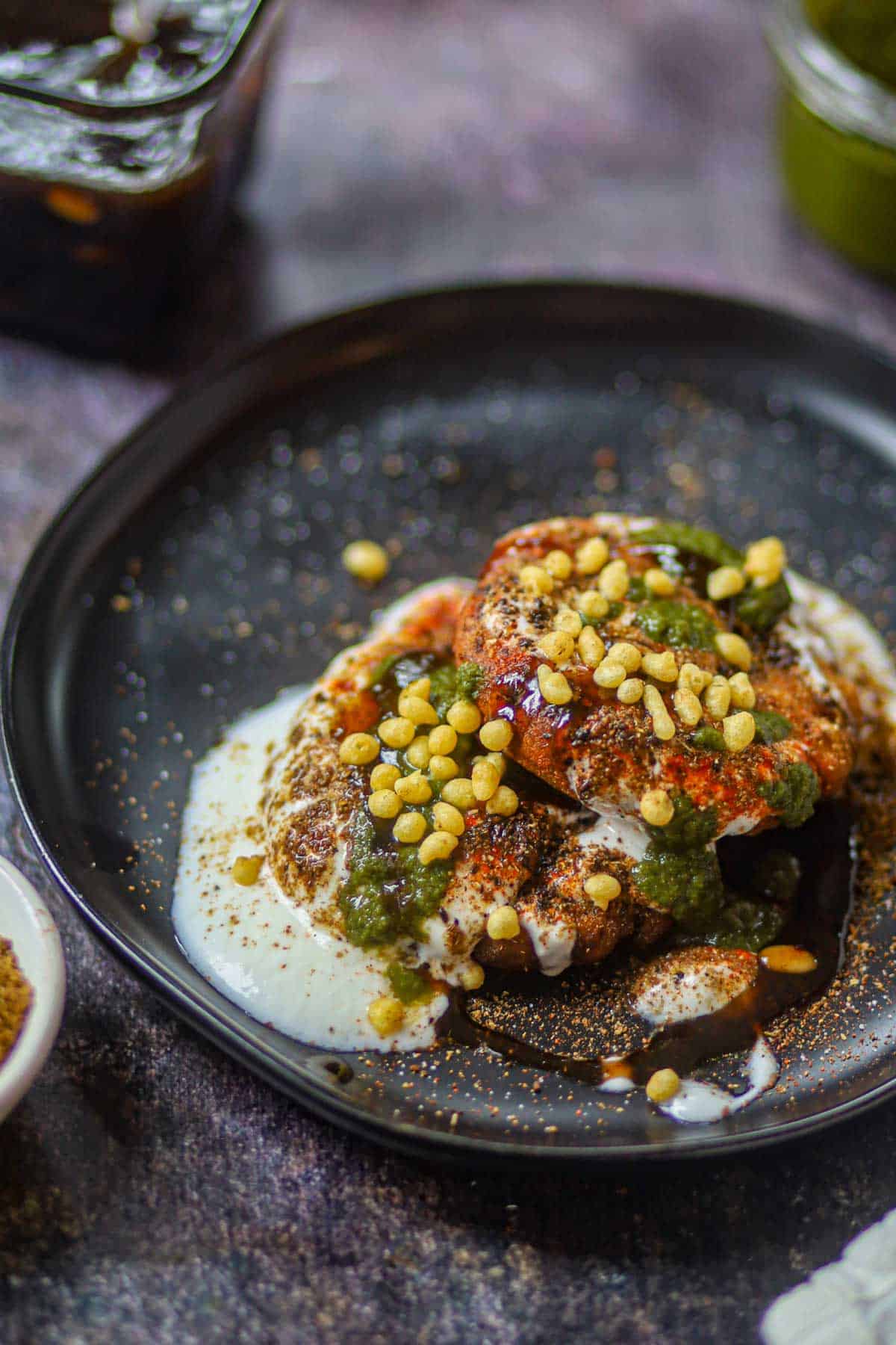 Close-up of aloo tikki chaat with yogurt, chutneys and boondi.