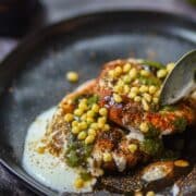 Spoon lifting crispy aloo tikki chaat topped with chutneys.