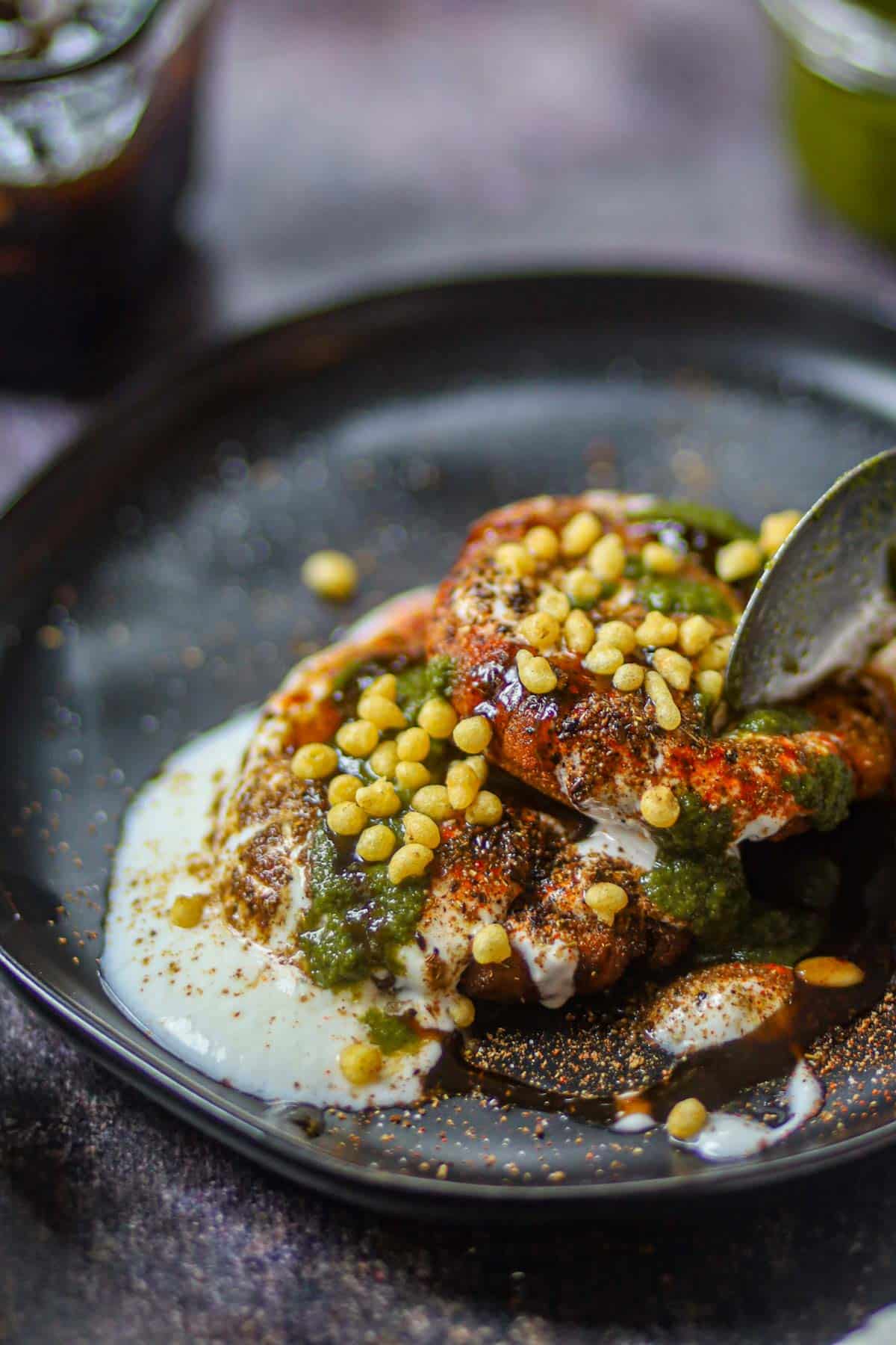 Spoon lifting crispy aloo tikki chaat topped with chutneys.