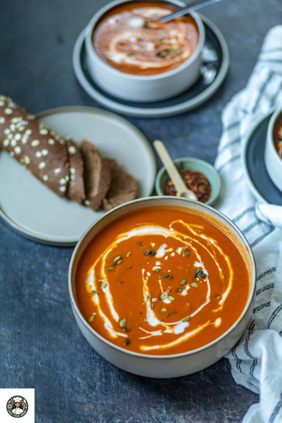Overshot image of tomato soup with coconut milk in a big white bowl garnished with coconut milk, basil, and pumpkin seeds with bread on the side.