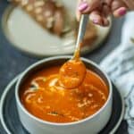 Image a spoonful of coconut milk tomato soup with brown bread.
