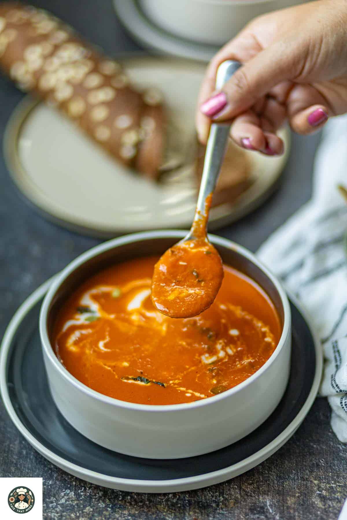 Image a spoonful of coconut milk tomato soup with brown bread.