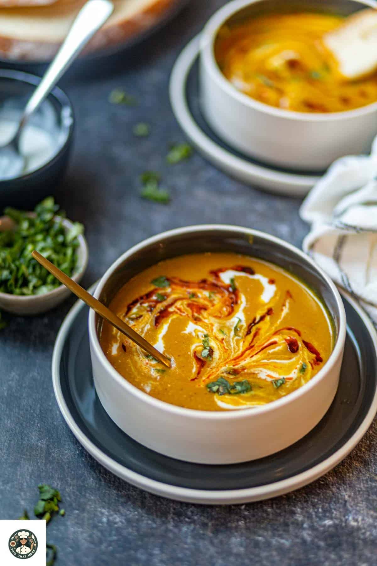 Image of spiced carrot & lentil soup in a white bowl over a blue plate with golden soup in the bowl with cilantro on the side.