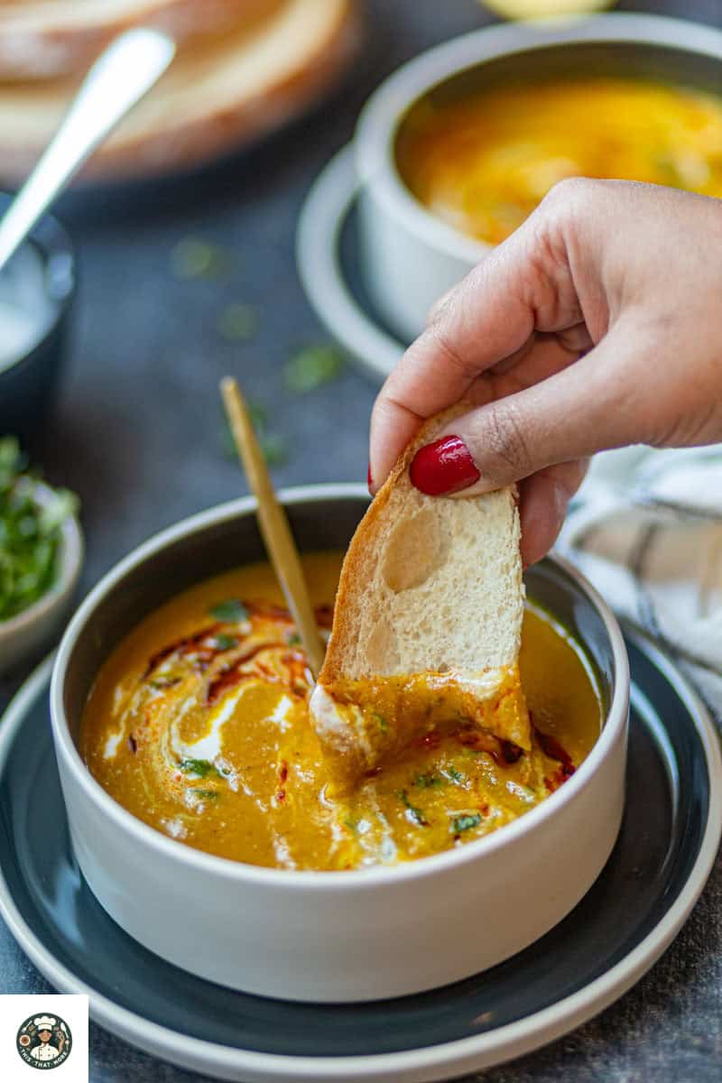 Overshot image of olive bread dipped in spiced carrot & lentil soup.