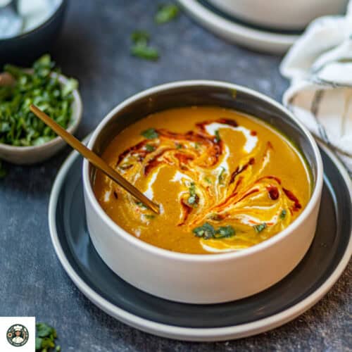 Featured image of spiced carrot & lentil soup which is garnished with coconut milk, chili oil, and cilantro leaves.