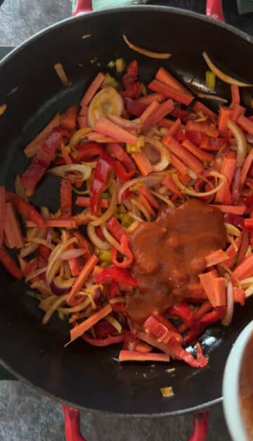 Red Thai curry paste being added to vegetables.