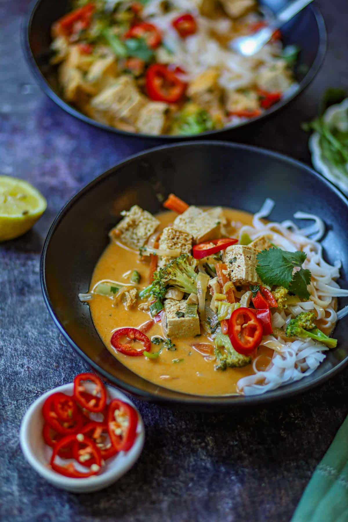 Bowl of Thai curry noodles with tofu, broccoli, peppers, rice noodles, and creamy coconut curry sauce.
