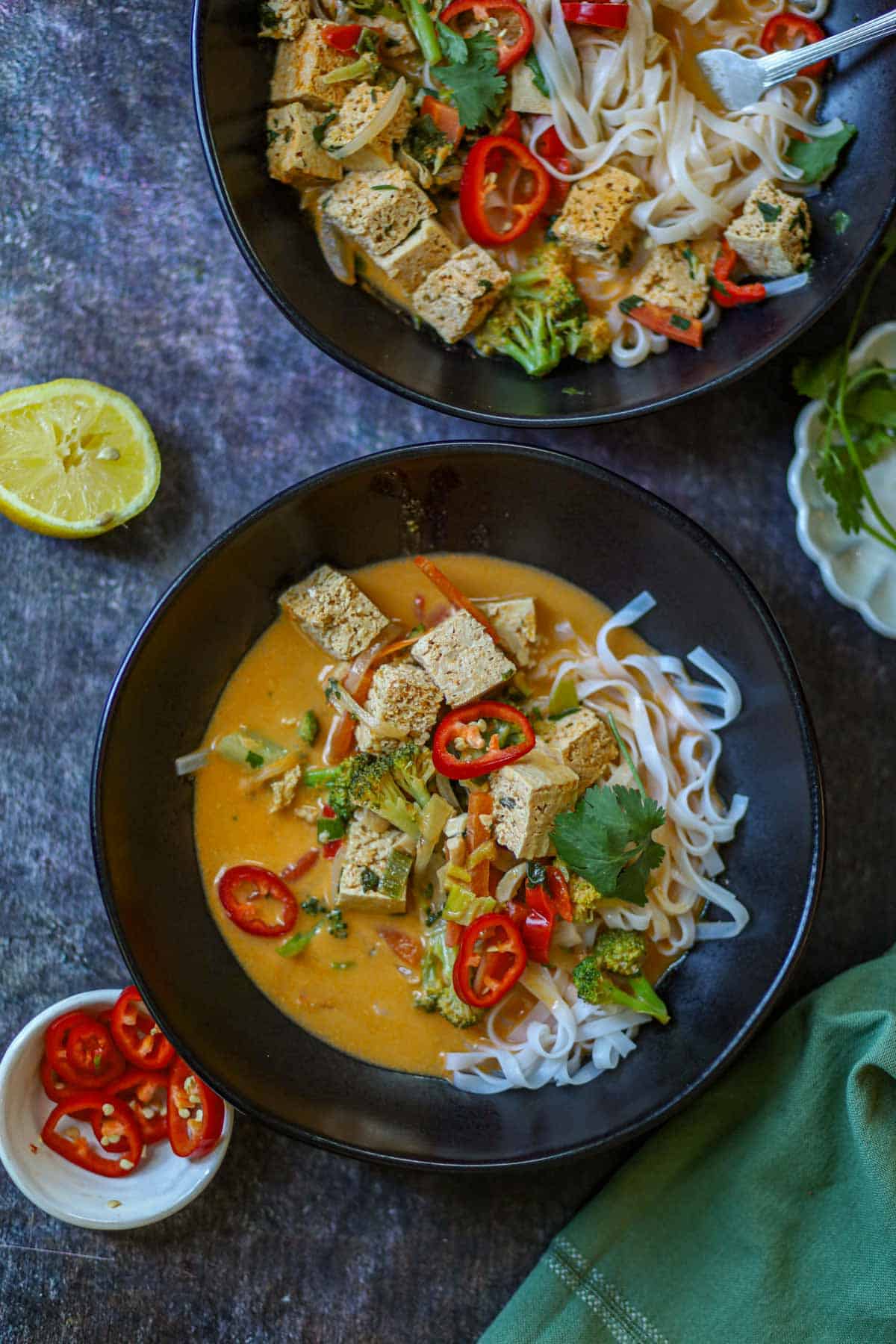 Two bowls of Thai curry noodles with tofu, vegetables, and creamy coconut curry sauce.