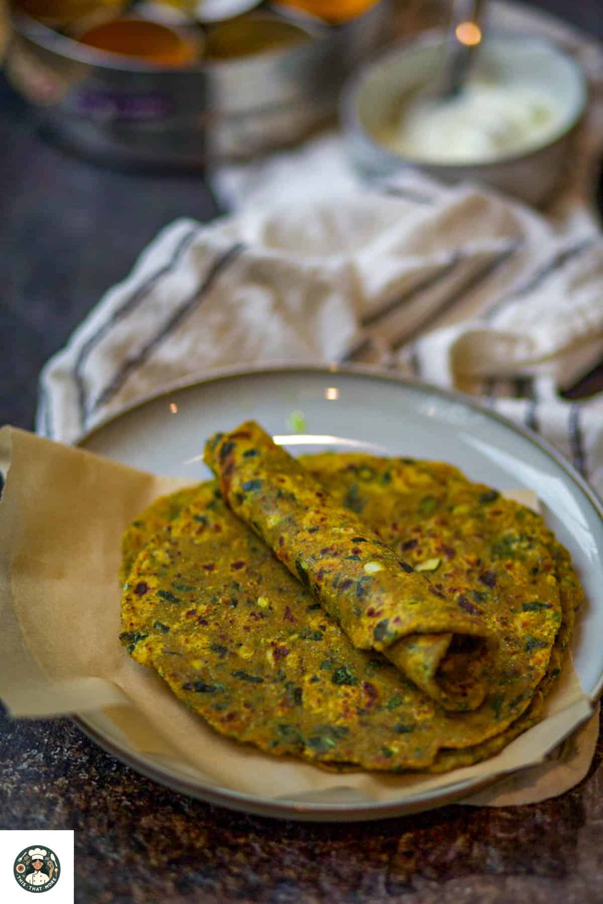 Image of methi roti which is rolled over another methi paratha on a white plate.
