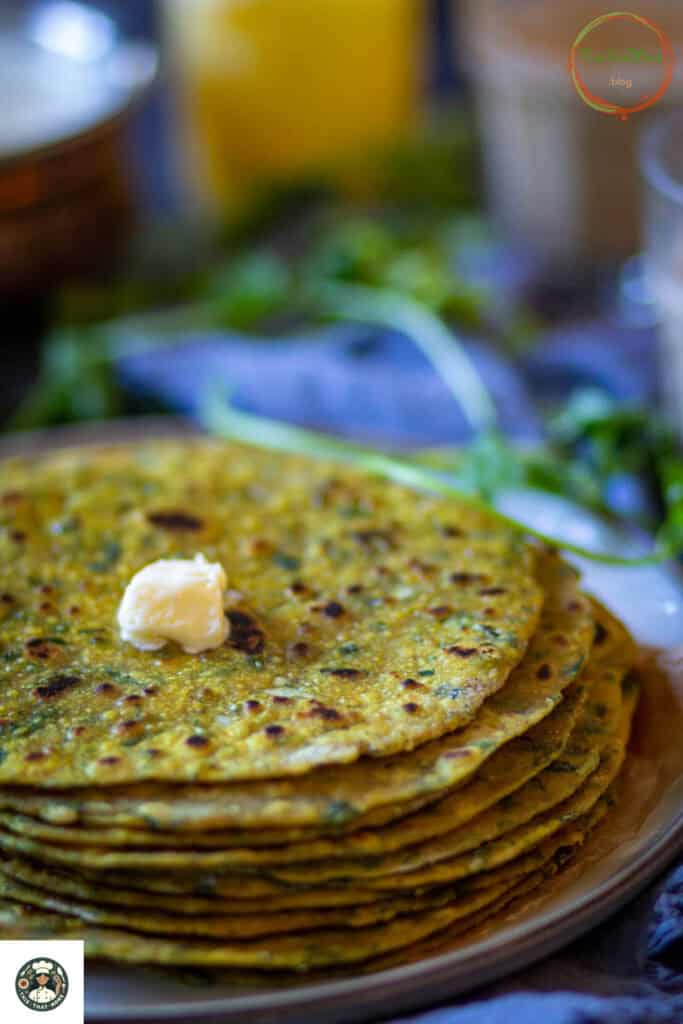 Side shot of stack of methi paratha recipe on a white plate with cilantro at the background. 