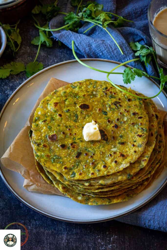 Imge of stack of methi parathas with a big spoonful of butter.