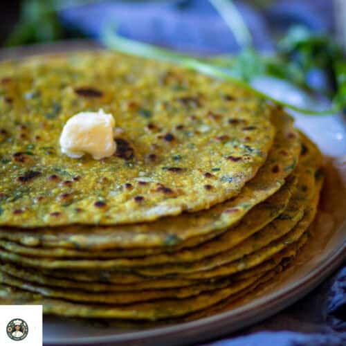 Overshot image of stack of methi paratha on a white plate with dallop of butter.