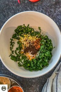 Image of a bowl with whole wheat flour, fenugreek leaves, ginger, garlic, and Indian spices in it.