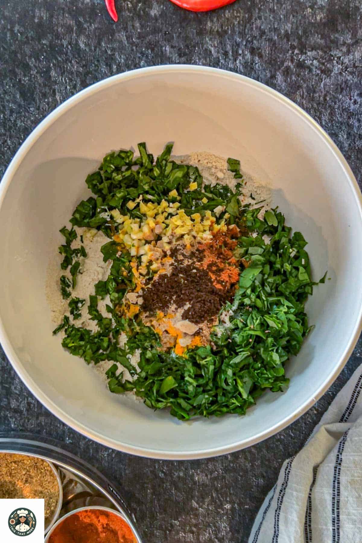 Image of a bowl with whole wheat flour, fenugreek leaves, ginger, garlic, and Indian spices in it.