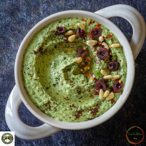 Cilantro jalapeño hummus served in a bowl with olives and pine nuts.