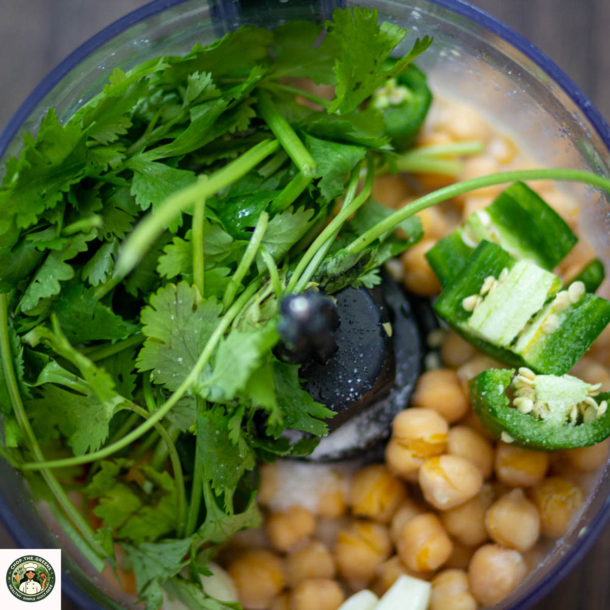 Cilantro, jalapeños, and chickpeas in a food processor before blending.