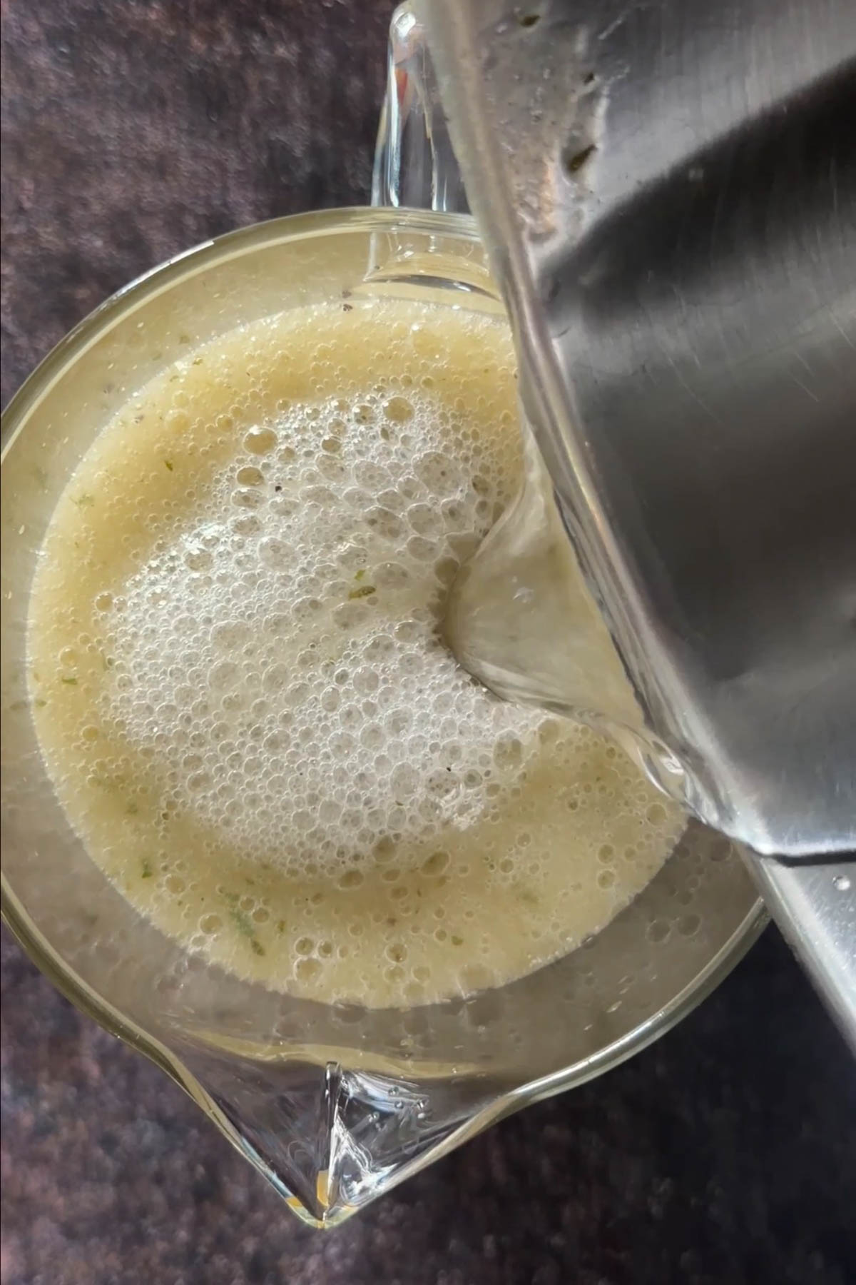 Freshly blended aam panna being poured into a glass pitcher.