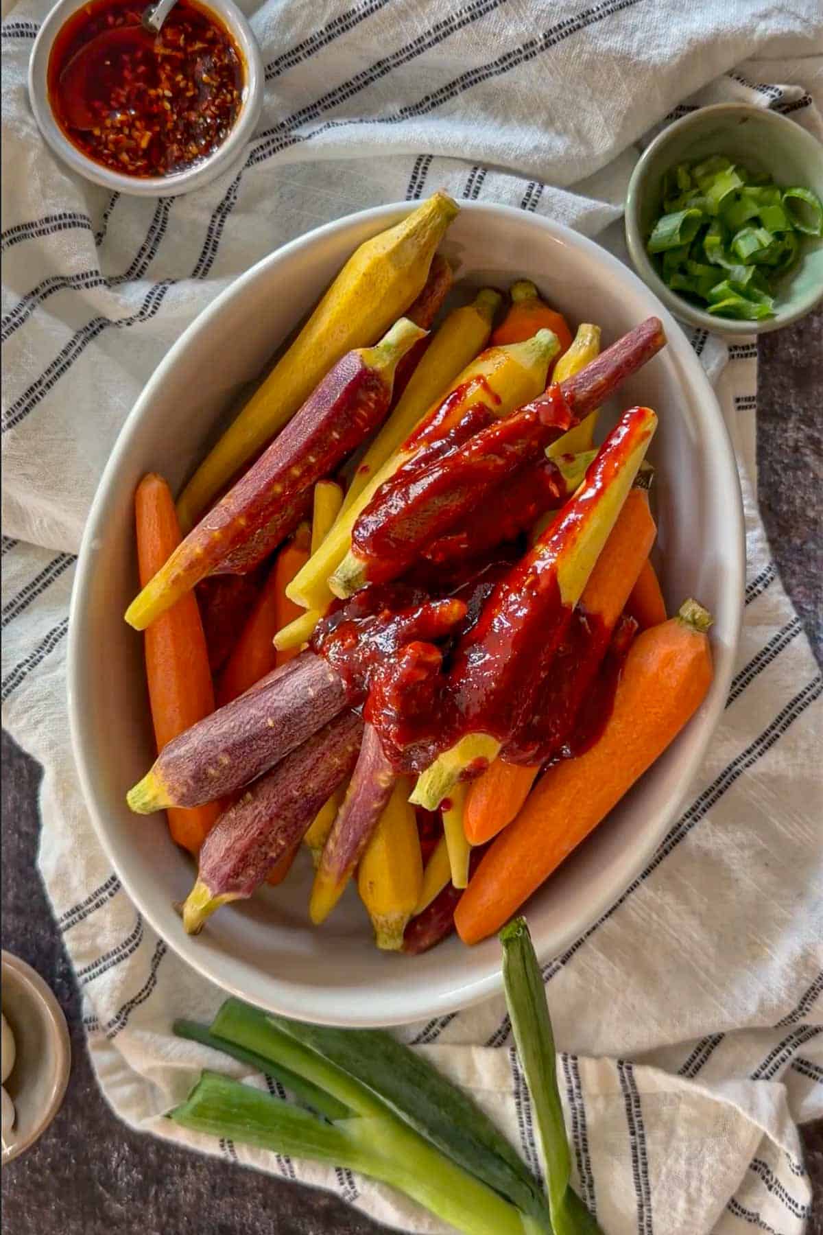 Fresh rainbow carrots topped with gochujang glaze in a white baking dish.