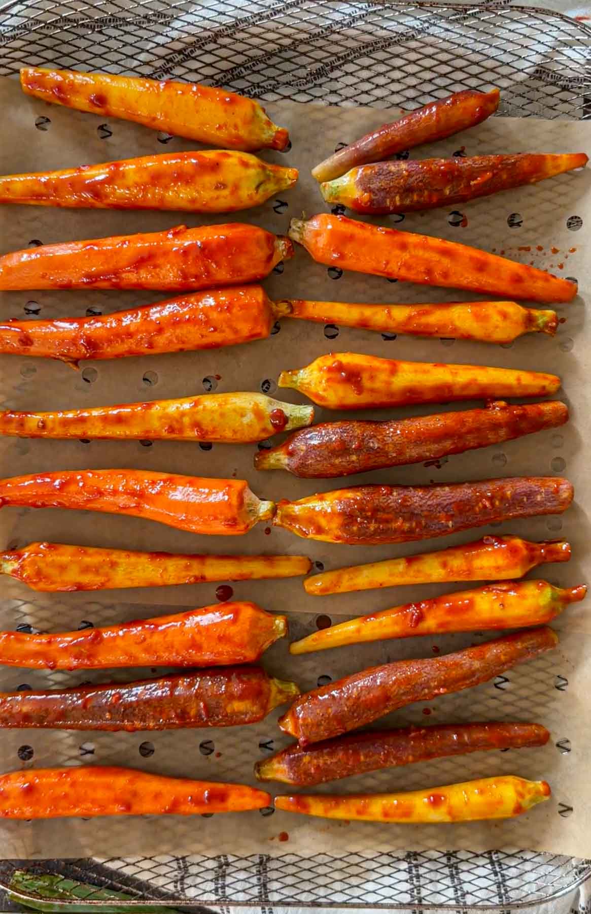 Gochujang-glazed carrots arranged in a single layer on parchment in the air fryer basket.