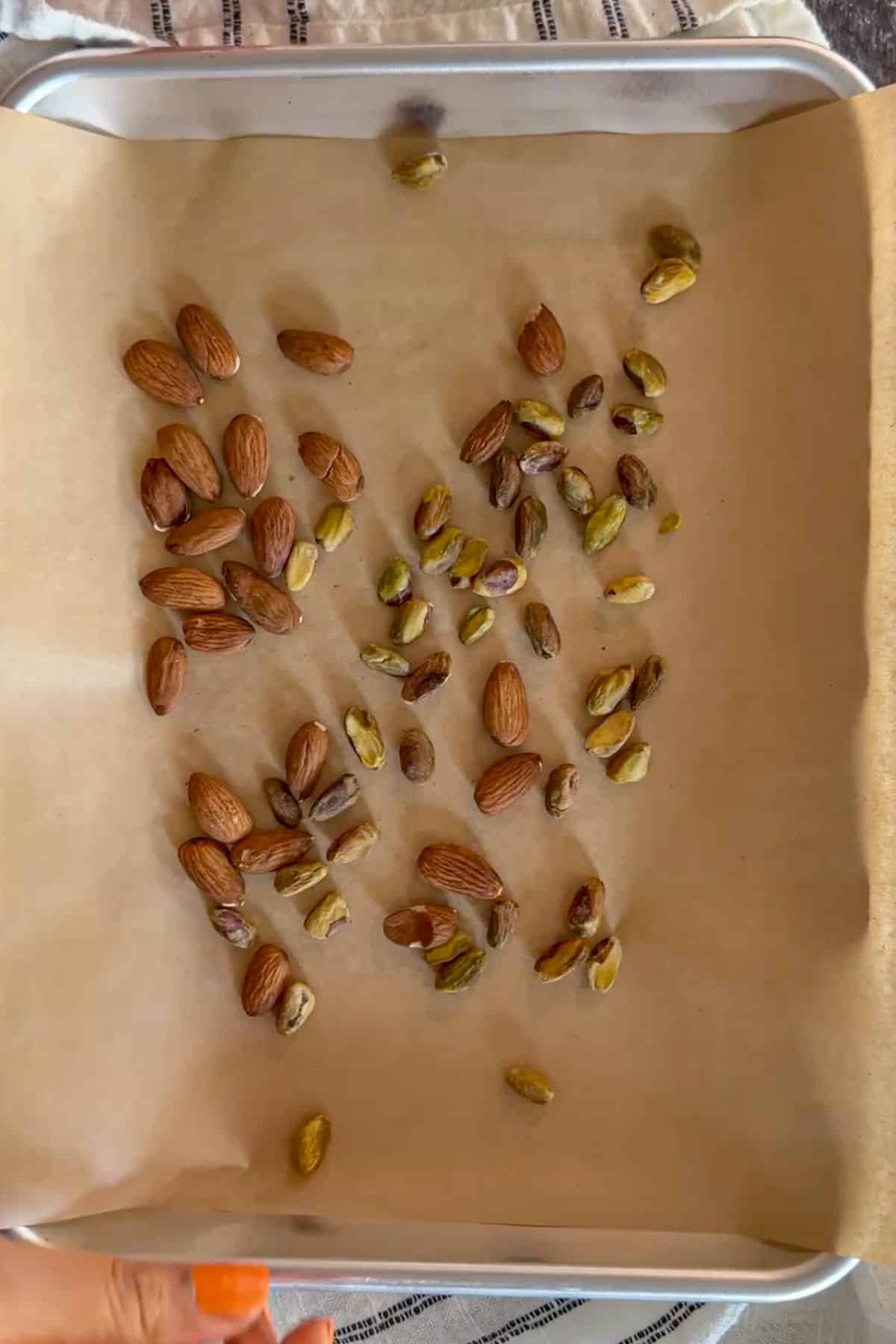 Almonds and pistachios spread on a baking sheet for roasting.