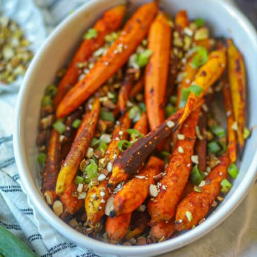 Air fryer gochujang carrots topped with chopped nuts and green onions in a white serving dish.