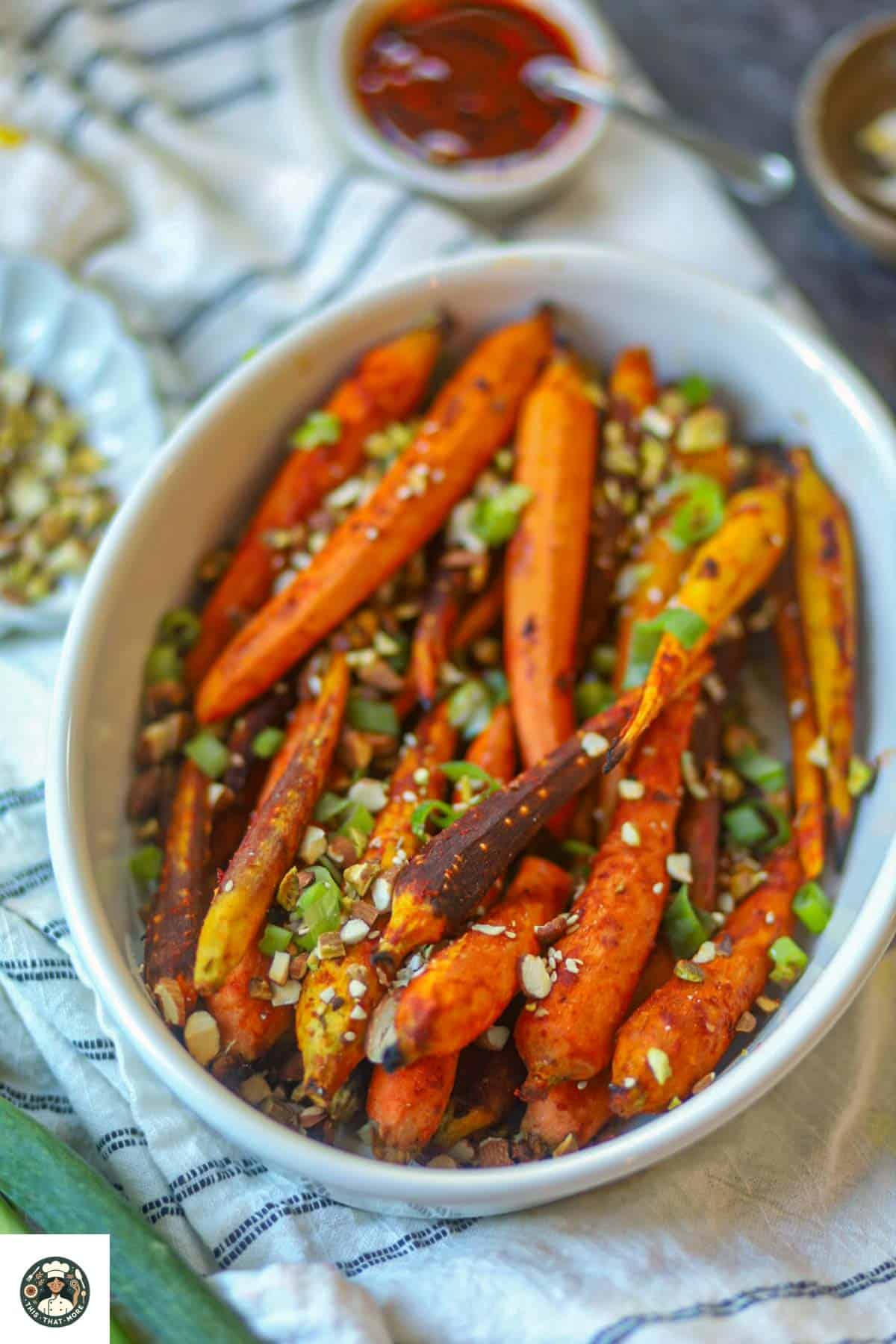 Gochujang glazed carrots served in a white bowl with nuts and scallions, Korean-inspired roasted carrot dish.