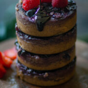 baked oats with blueberries stacked on a plate with chocolate syrup dripping from the top