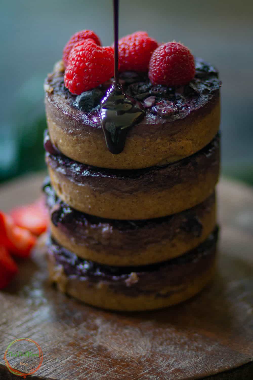 baked oats with blueberries stacked on a plate with chocolate syrup dripping from the top