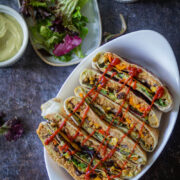 vegan crunchwrap supreme are lined a white bowl, drizzled with sriracha sauce