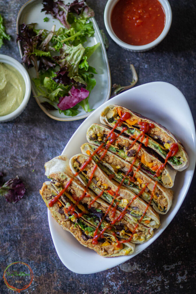 vegan crunchwrap supreme are lined a white bowl, drizzled with sriracha sauce