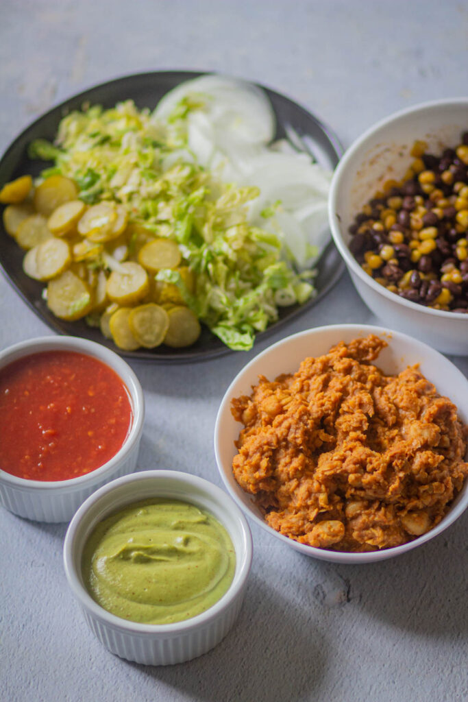 all the ingredients in bowl includign chickpea filling, veggies, black bean & corn filling, cream sauce, salsa, and onions