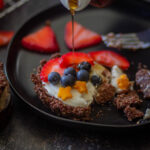 mini fruit tar on a black plate topped with blueberries and strawberries