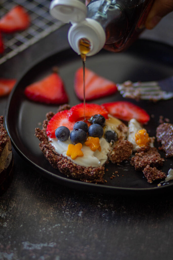 mini fruit tar on a black plate topped with blueberries and strawberries