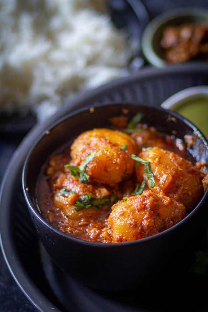 dum aloo recipe in a black bowl with some boiled rice