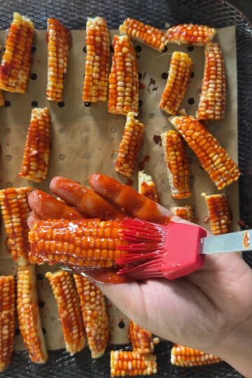 Brushing gochujang glaze over corn ribs before air frying.