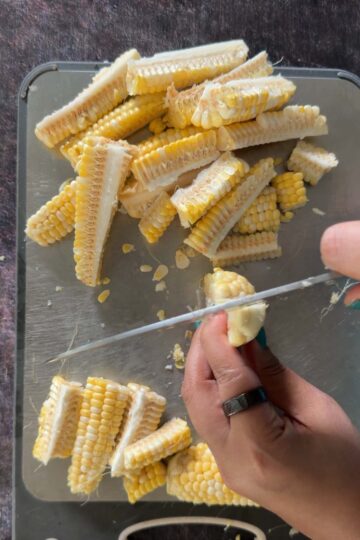Corn cob being quartered lengthwise into four corn ribs.