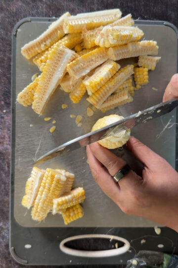 Cutting a corn cob lengthwise into corn ribs with a chef's knife.