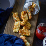 zucchini fries laying flat on the wooden cutting board with ketchup