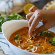 Hand dipping naan into creamy paneer curry.