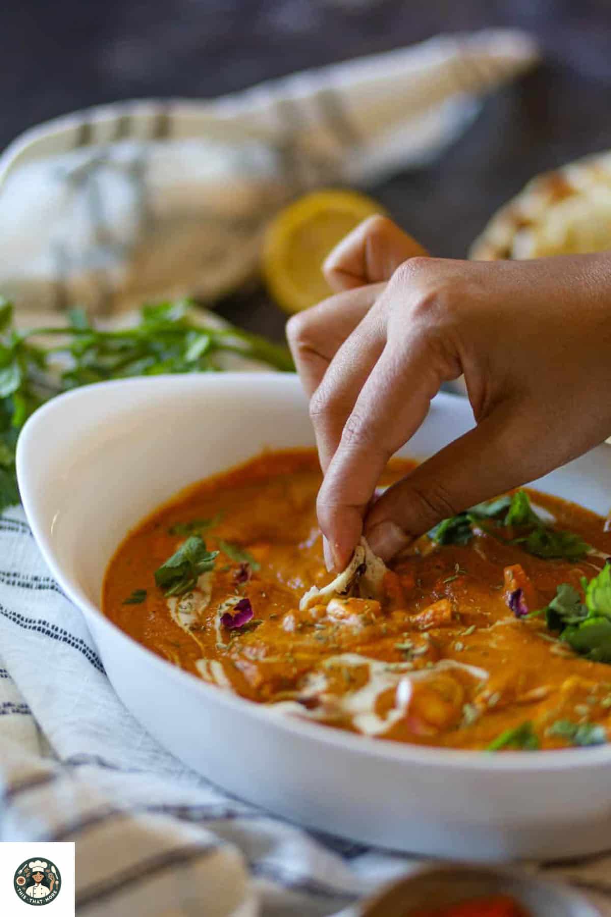 Hand dipping naan into creamy paneer curry.
