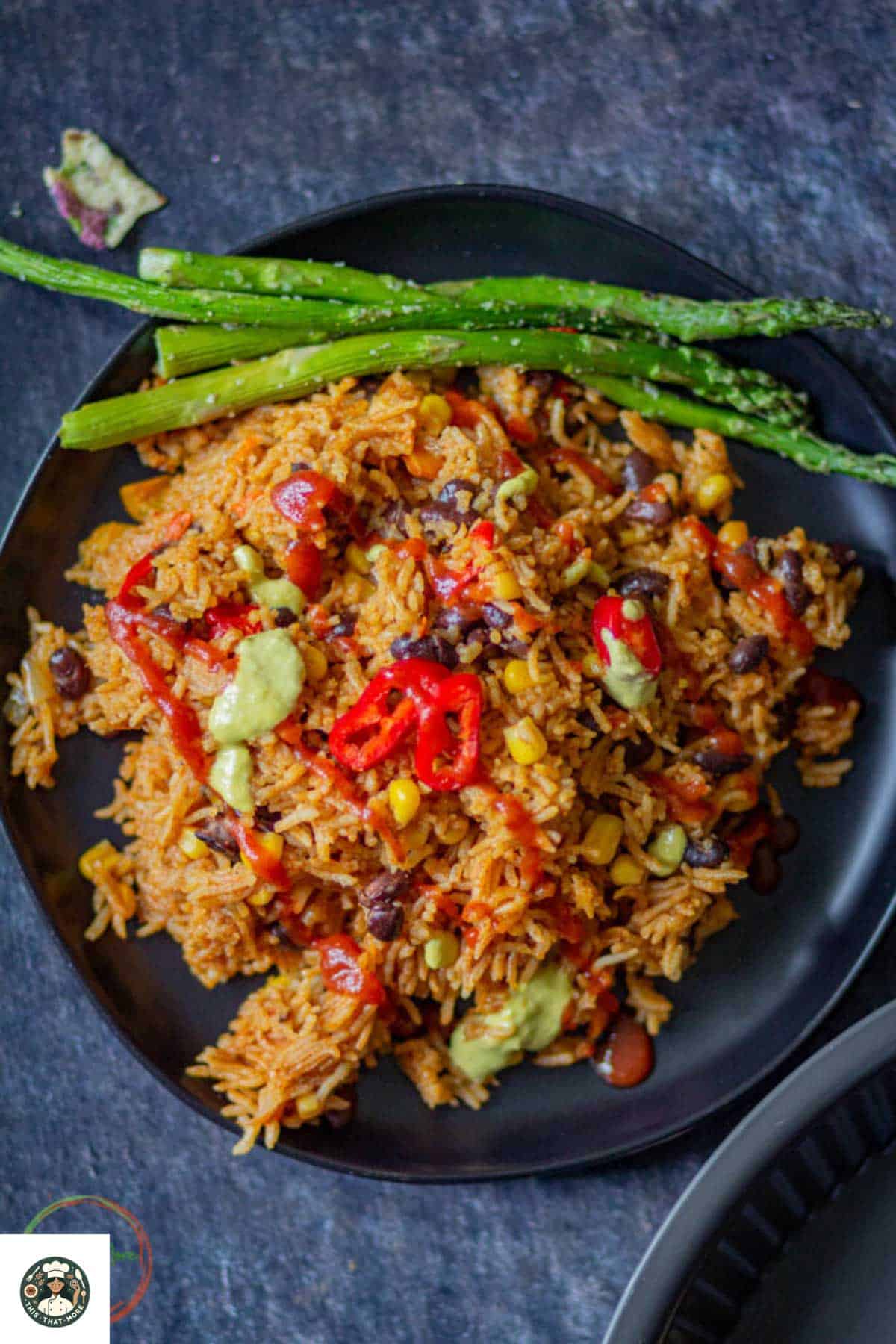 Image of a big plate of vegetarian enchilada rice on a black plate and it is served with grilled asparagus.