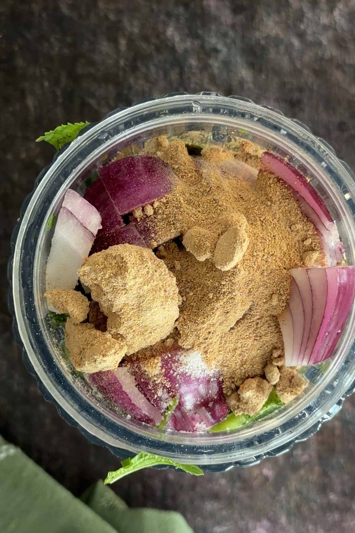 Onion, herbs and amchur added to blender for green chutney.