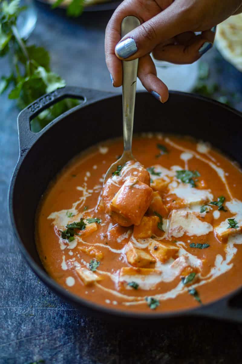 Taking a big spoon full of paneer butter masala, garnished with cream and cilantro.