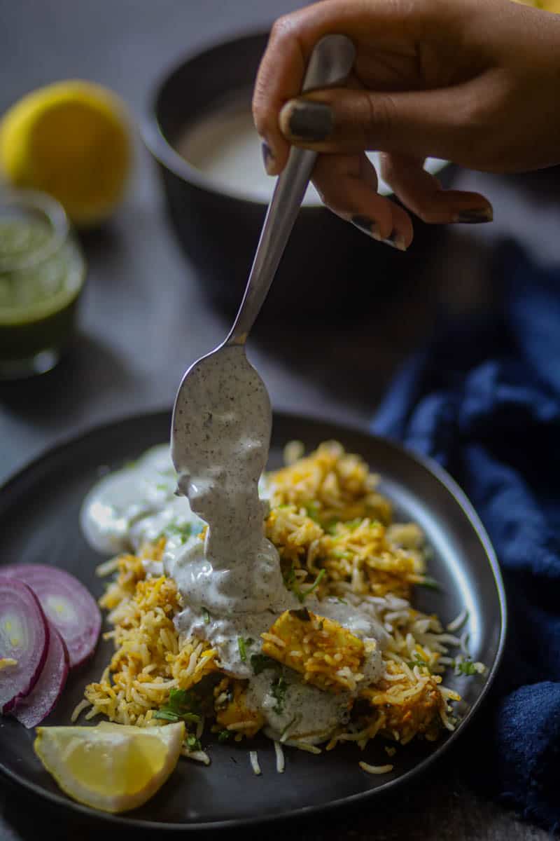 Adding yogurt over the biryani in a black plate.
