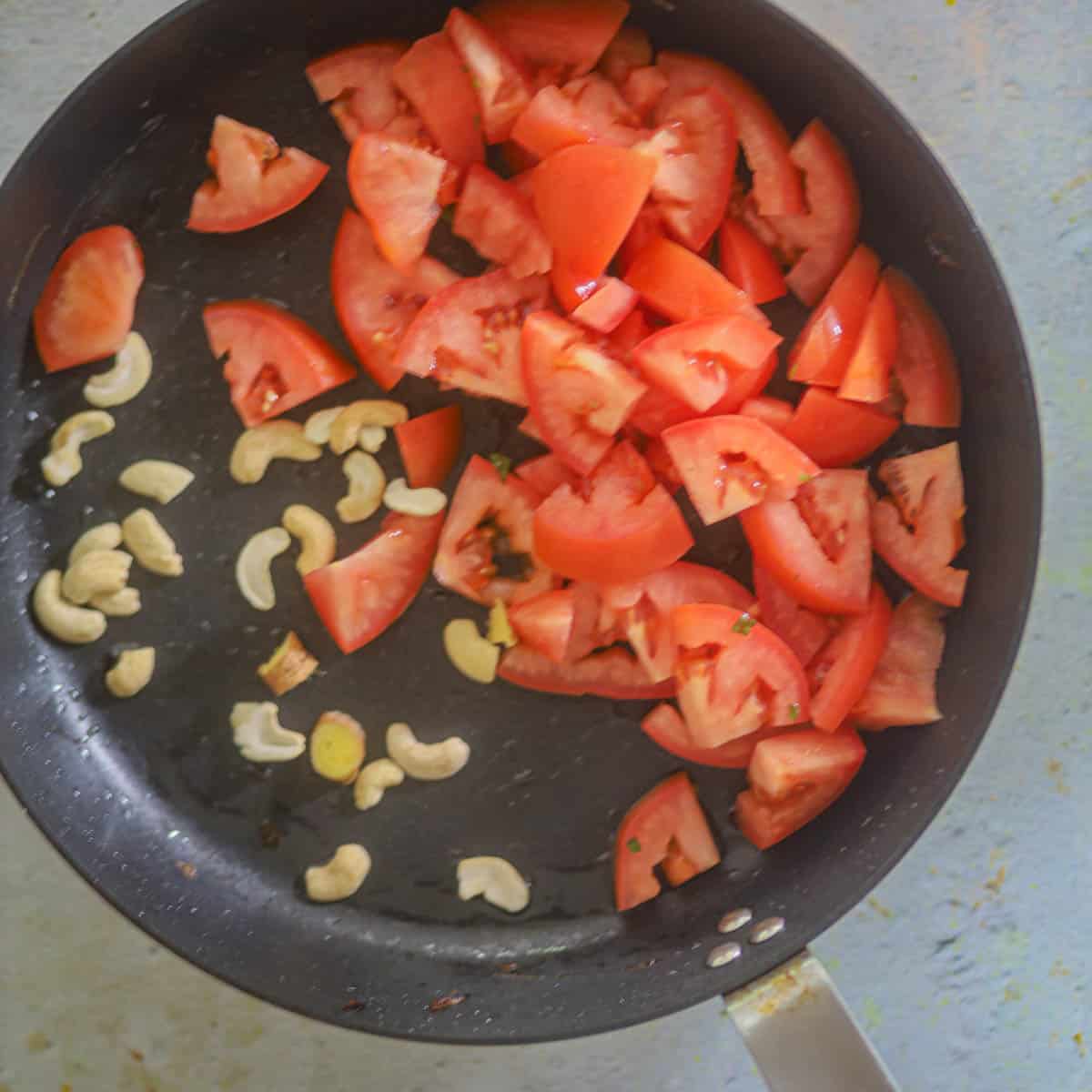 Add tomatoes, cashews, ginger and garlic in a pan.