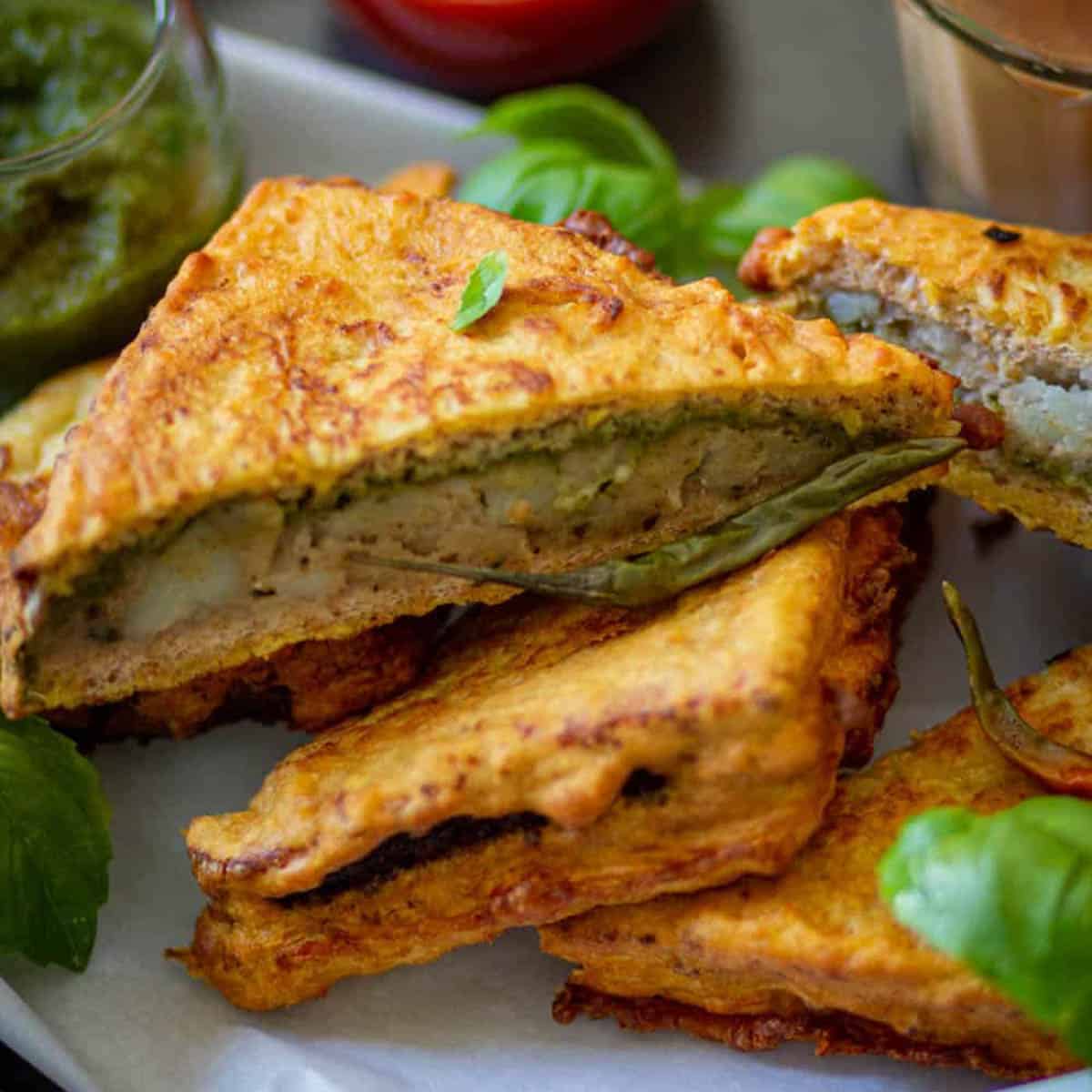 Bread Pakora on a plate, garnished with green chili and basil leaves.