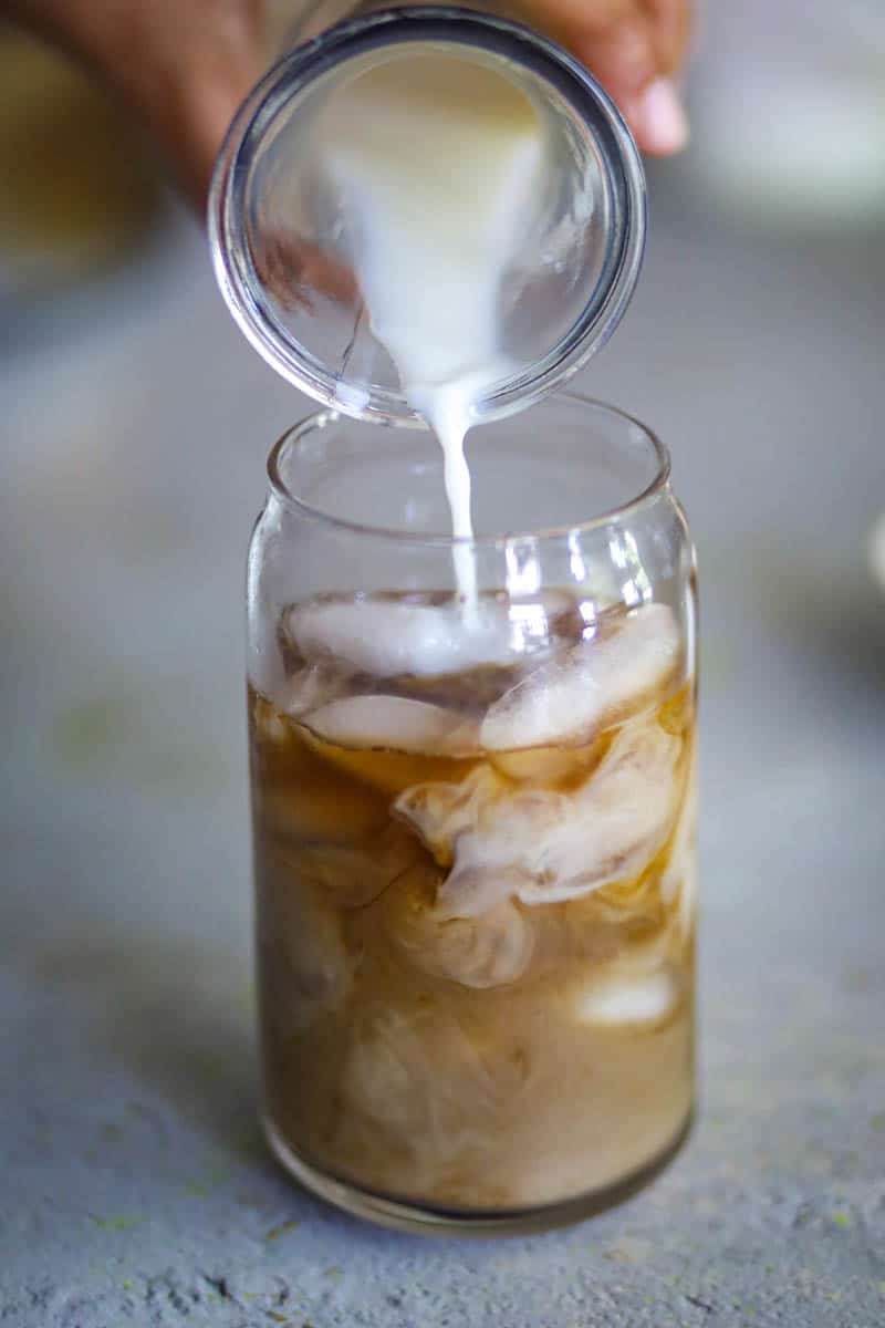 Pouring milk over the coffee in the glass.